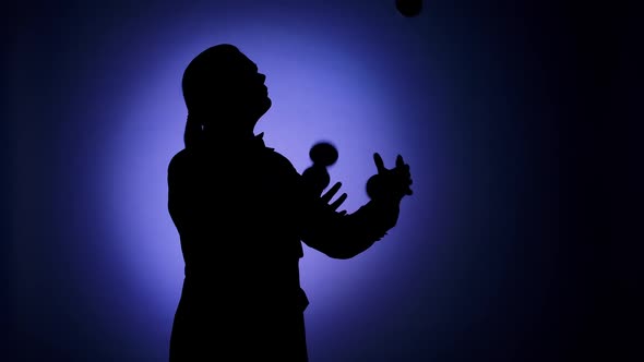 Black Silhouette of a Man Juggling Balls in the Spotlight