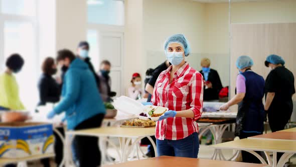 Female Volunteer in Mask and Gloves Holds in Hands a Foam Lunchbox with Charity Hot Meal