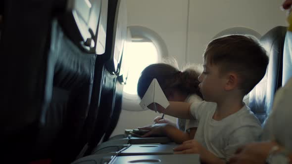 Children Sitting By Aircraft Window and Playing with Little Paper Plane During Flight on Airplane