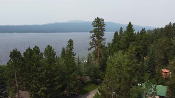 Drone shot revealing Payette Lake through the pine trees on a smoky day in McCall, Idaho. This cinem