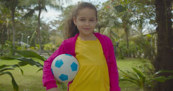 A Cute Little Girl with a Soccer Ball in His Hand Smiling Looking at the Camera Is Preparing To Play