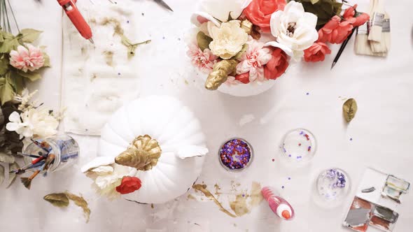 Top view. Mother and daughter painting face of an unicorn and decorating craft pumpkins with flowers