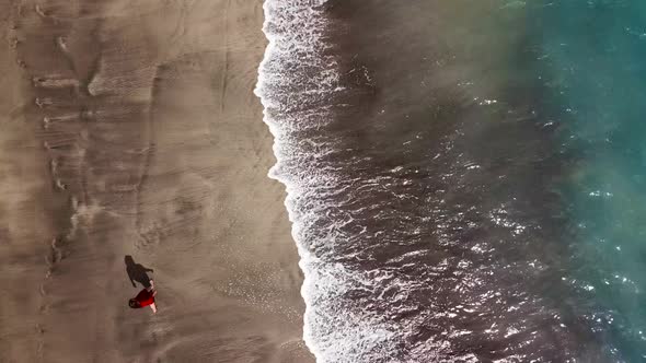 Top View of a Woman in Red Dress Walking Barefoot Along Wet Sand Ocean Beach