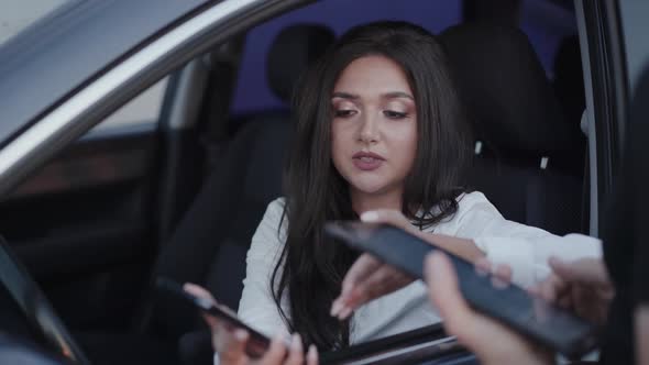 Confused Girl in Car with Smartphone Talks with Someone with Gadget and Smiles