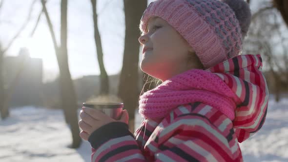 Child Girl Kid Drinking Hot Drink Tea From Cup on Snowy Road in Winter Park Christmas Holidays