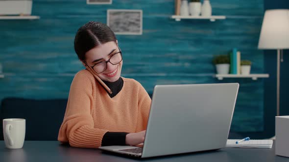 Young Woman Talking on Phone Call and Using Laptop at Home Desk