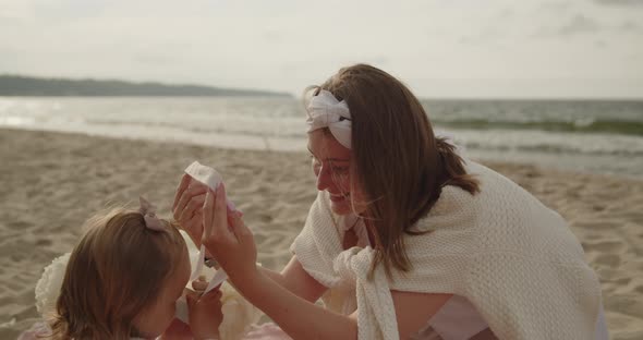 Mother and Baby Daughter Sit on the Beach Near the Sea Playing Together