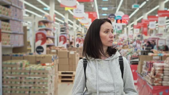 Pretty Young Woman Walks Through the Supermarket Hall with a Cart and Smiles