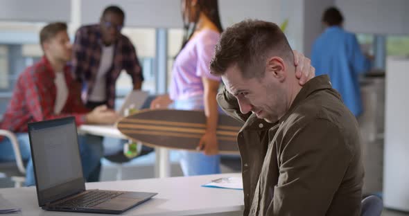 Young Man Massaging Aching Neck Having Health Problems After Computer Work in Modern Office