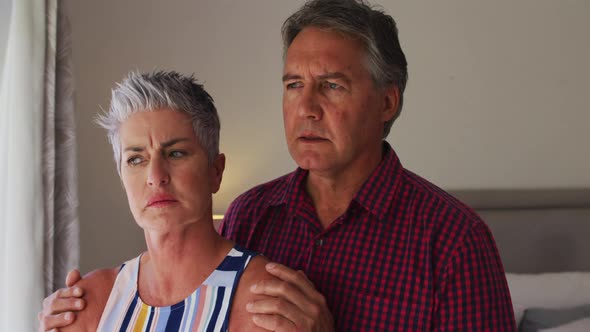 Stressed caucasian senior couple talking to each other while looking out of the window at home