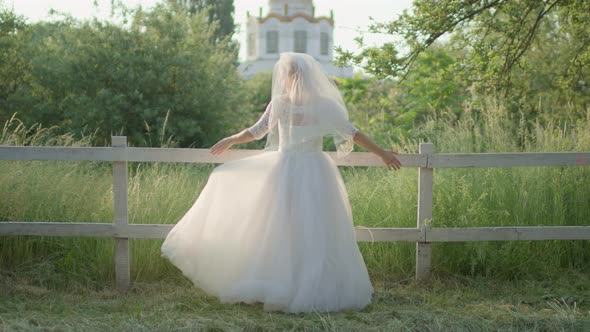 Back of Bride in White Wedding Dress Standing Near the Church at Sunrise