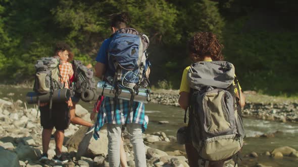 Rear View of Diverse Multiracial Tourists with Backpacks Backpacking By Mountain River