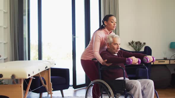 Video of happy biracial female physiotherapist exercising with caucasian senior man