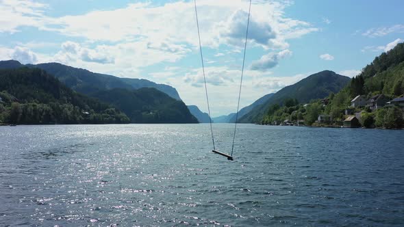 Tall swing moving slowly from side to side with amazing scenic Veafjorden in background - Static aer