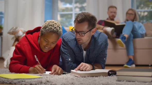 Happy Multiethnic Students Preparing for Exams Together Lying on Floor in Dorm Room