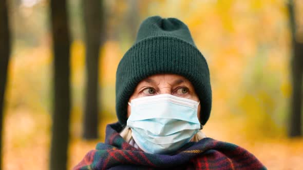 An Elderly Woman 50s Wearing Warm Clothes and a Protective Medical Mask Looks at the Camera
