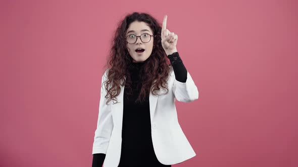 The Young Woman Shocked with Curly Hair Points Upwards Recommending Something
