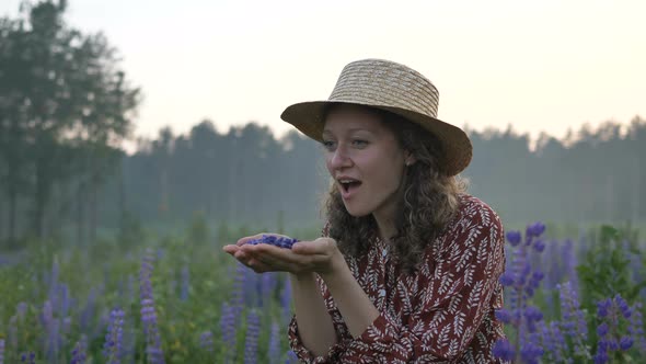 Woman in Straw Hat Blows Off Petals of Violet Flowers