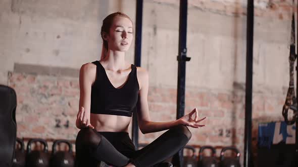 Fit Young Woman Meditating In Gym. Practicing Yoga at Fitness Studio.