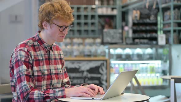 Young Redhead Man Reacting to Loss on Laptop in Cafe