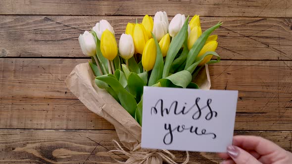 Put a card MISS YOU on a tulip’s bouquet on a wooden table top view 