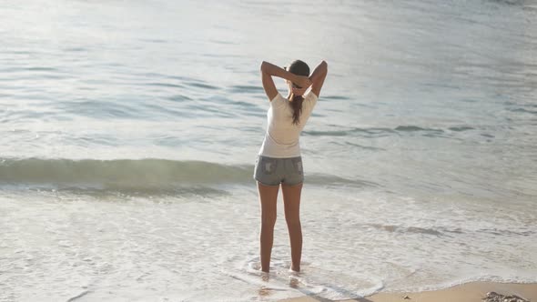 Backside View of Woman Looks at Ocean on Beach and Spreads Arms Wide Open