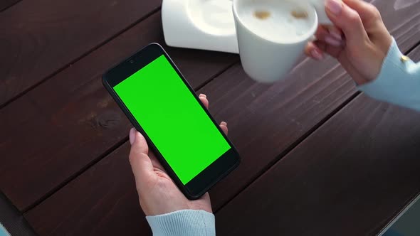 Womans Hand Use Green Screen Smartphone for Online Shopping at Cafe Table with Coffee Cup