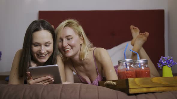 Smiling Young Girls Using Tablet Pc Lying in Bed