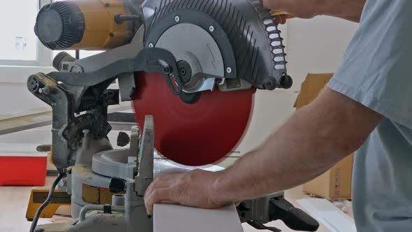 Worker Cuts Wood Baseboard on the Power Miter Saw
