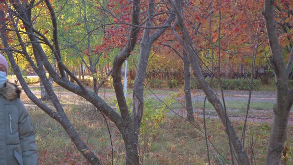 A woman in a medical mask walks through the autumn park and coughs.