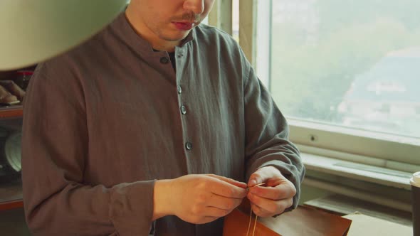 A Young, Experienced Tailor's Apprentice Threads a Needle for Sewing a Genuine Leather Product in a