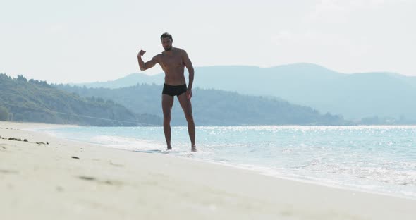 The Handsome Man with a Perfect Athletic Body in Swimming Trunks Having Fun on a Deserted Beach in