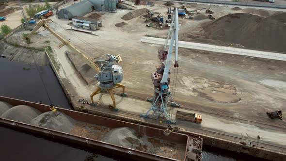 Large Harbor Cranes Onshore at the Quay Unload a River Gravel Barge Onto a Large Pile