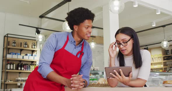 Video of happy diverse female owner and male waiter working with tablet at cafe shop