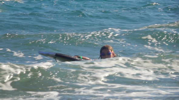 Little Cheerful Girl is Riding on the Swimming Board in a Splashing Sea