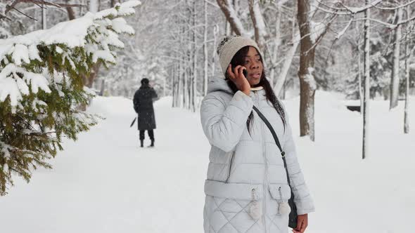Young Black Woman Talks on Her Phone in Winter Forest and Finds Her Friend Behind Her