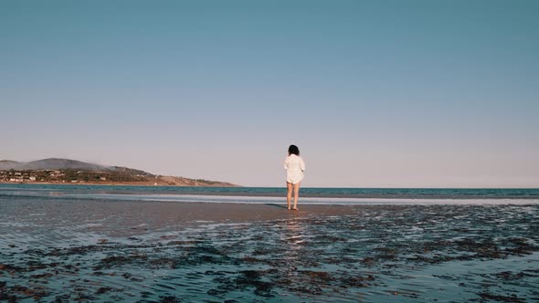 A woman walks barefoot on the beach