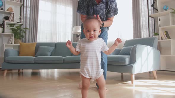 Father Encouraging Smiling Baby Son To Take First Steps And Walk At Home