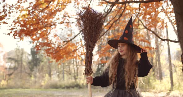 Cute Little Girl with Long Hair Looking Like a Witch in a Special Dress and Hat in the Autumn Forest