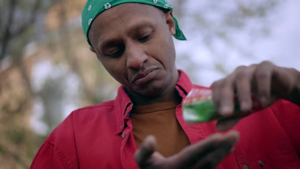 Closeup Portrait of Concentrated African American Gardener Pouring Seeds From Package in Hand