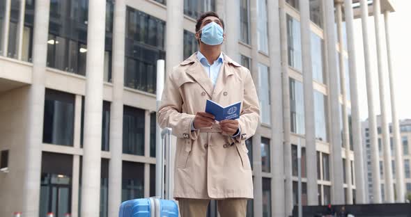 Man in Safety Mask Holding Vaccination Certificate for Covid19 Standing with Suitcase Outdoors