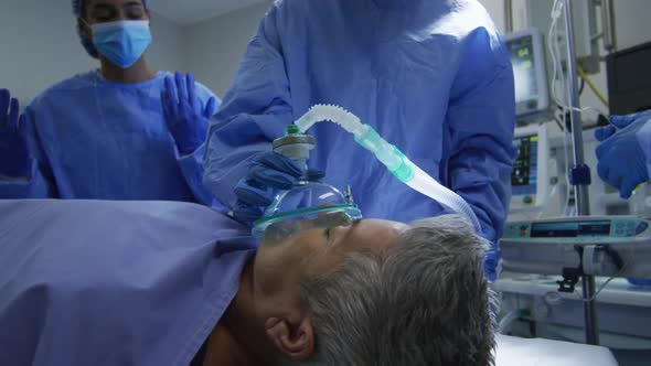 Mixed race surgeons wearing protective clothing putting patient to sleep in operating theatre