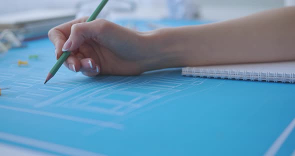 A young woman works and studies architecture from blueprints. She draws with a pencil in a notebook