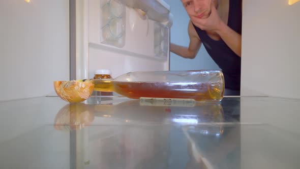 man looks into an empty refrigerator and takes out bottle of alcohol. Alcoholism