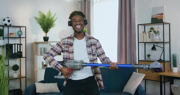 Black-Skinned Guy in Headphones Playing on Vacuum Cleaner Like a Guitar During House cleaning