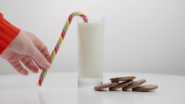 Caucasian Female Hand Putting Christmas Candy Cane on Glass with Milk for Santa