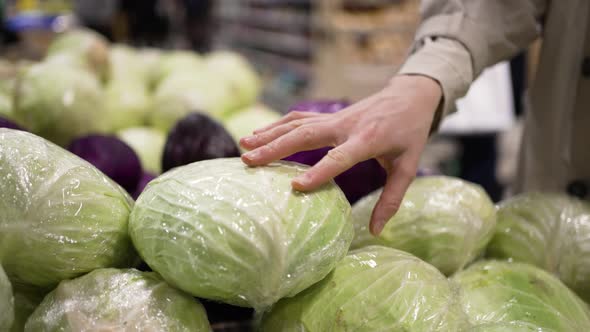 Woman Takes Green Cabbage From Heap in Supermarket