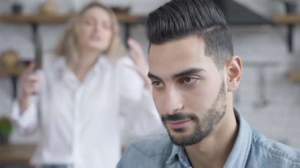 Headshot Portrait of Young Handsome Bored Man Listening to Blurred Angry Woman Arguing at Background