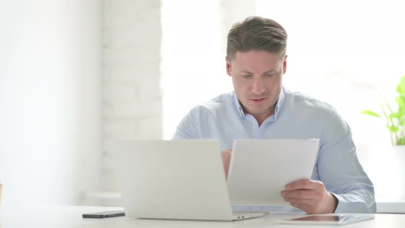 Man with Laptop Having Loss while Reading Documents