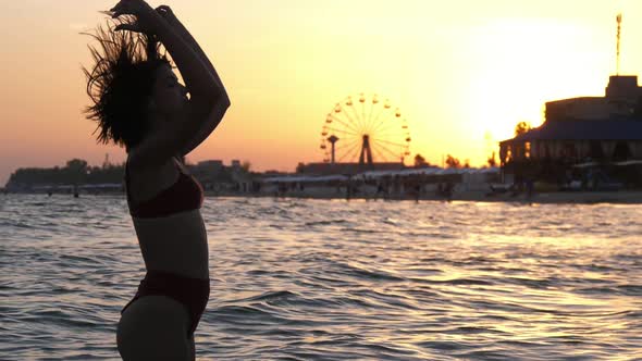 Romantic Girl Raising Her Hair Up on a River Bank at Shining Sunset in Slow Motion